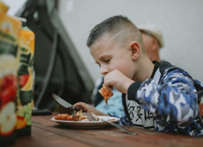 Young boy savoring a grilled chicken meal during an outdoor barbecue.