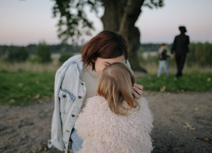 A tender moment between mother and daughter outdoors in a grassy field at twilight.