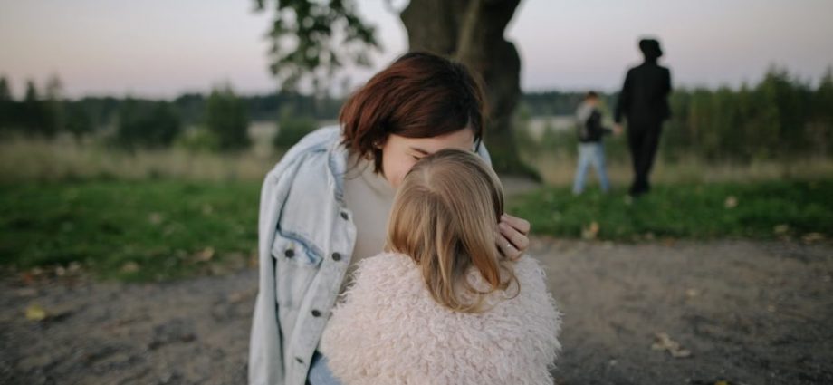 A tender moment between mother and daughter outdoors in a grassy field at twilight.